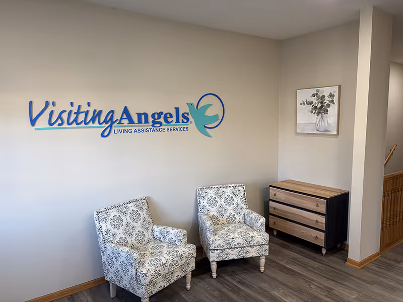 Lobby area with Visiting Angels sign, two patterned chairs, and a wooden dresser.