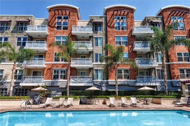 Exterior view of Chapman Commons residential complex with a pool, lounge chairs, and palm trees.
