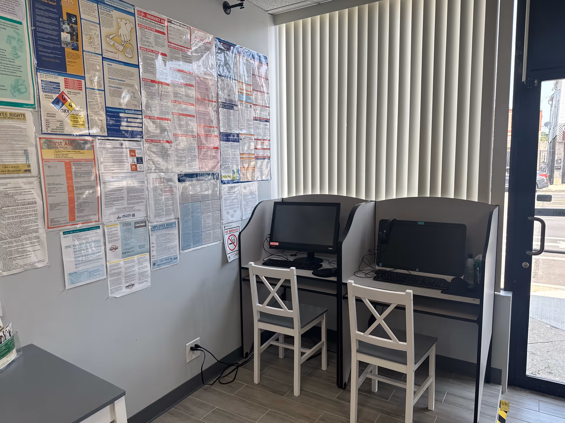 Two computer desks with chairs sit against a wall covered in posters.