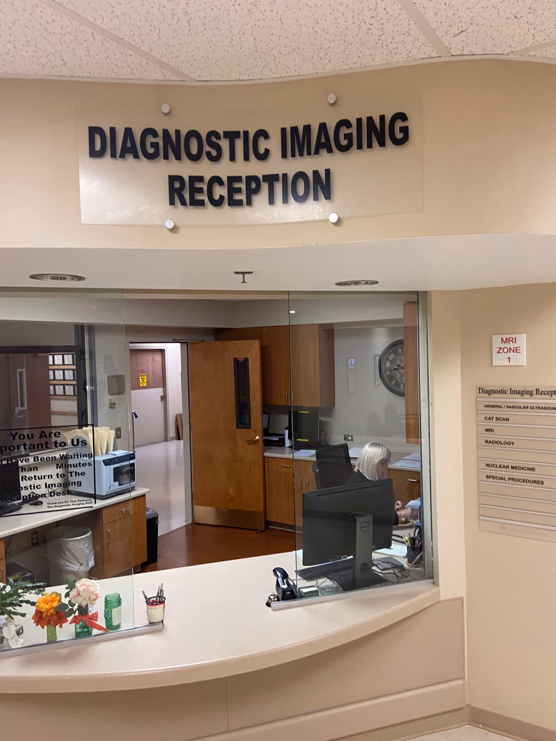 Interior reception area with glass window, desk, computer, and diagnostic imaging sign at Almighty Homecare Services.