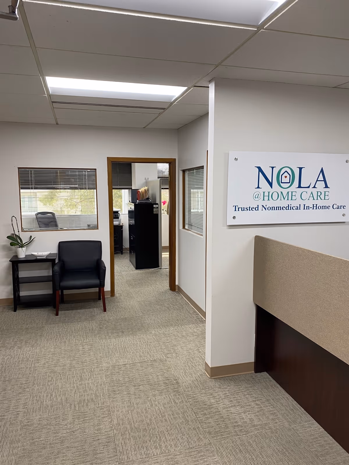 Interior lobby of Nola @ Home Care featuring seating, plant, and a sign.