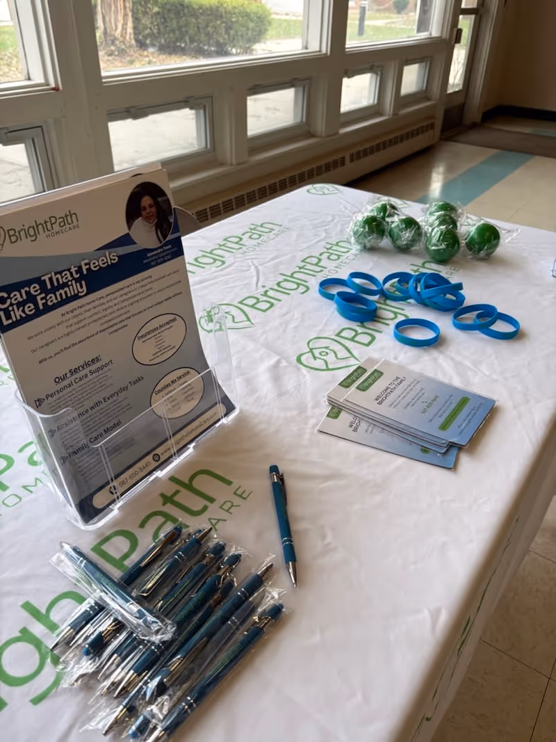 Promotional table with BrightPath Home Care brochures, pens, and wristbands inside a bright indoor space.