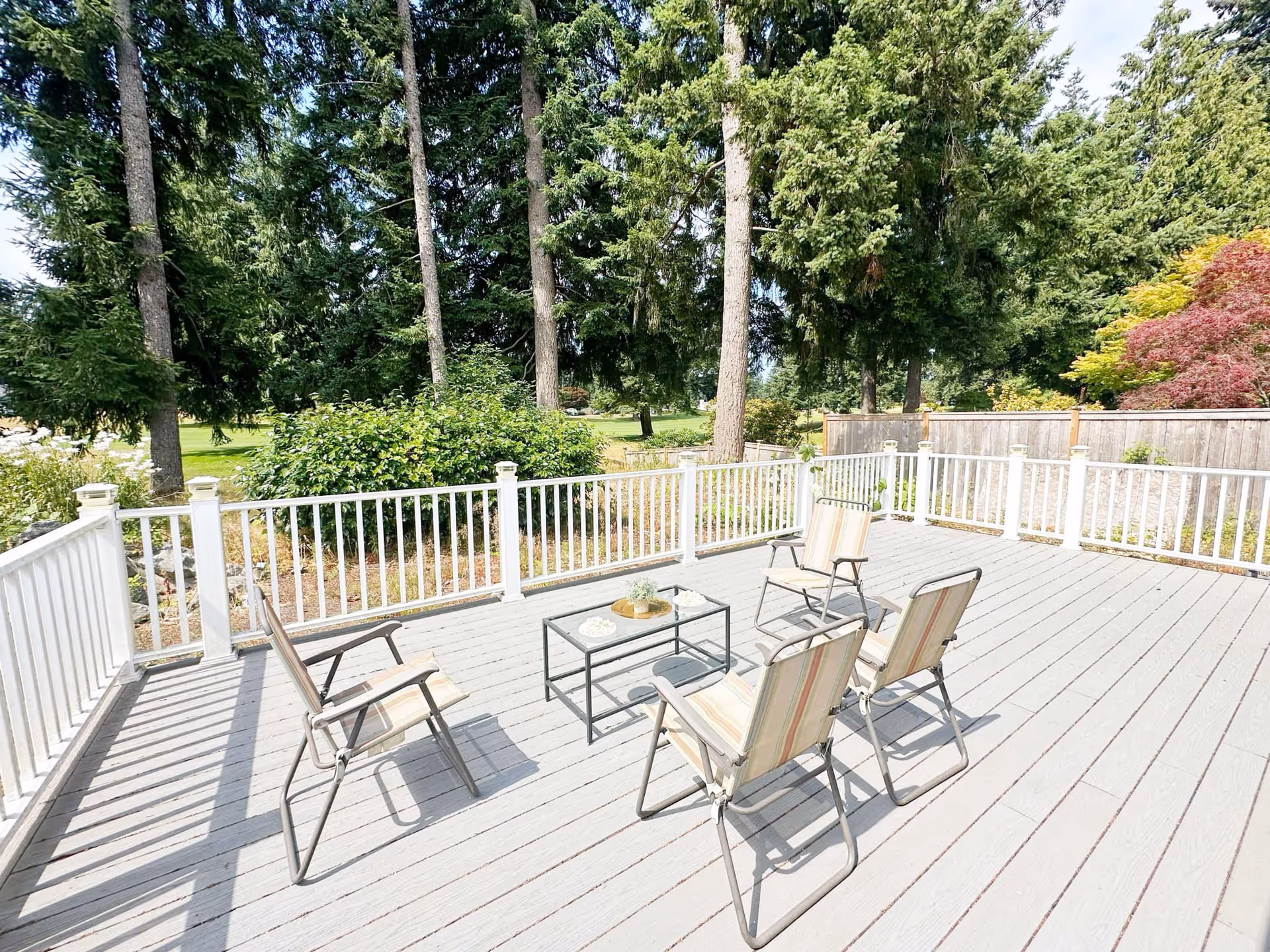 Sunny wooden outdoor deck with chairs arranged around a table and trees beyond.