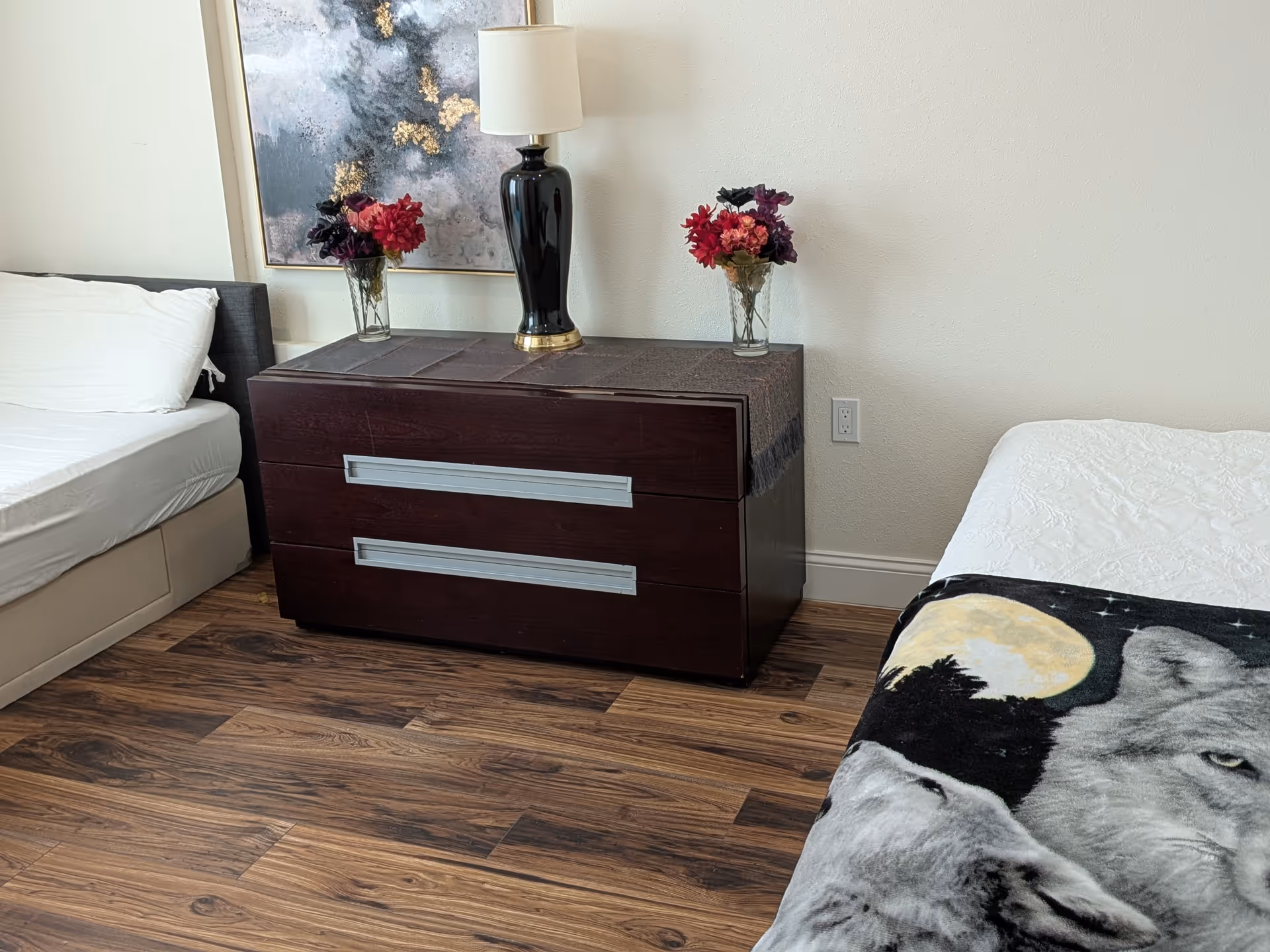 Bedroom with a dark dresser, two beds, a lamp, and vases of flowers.