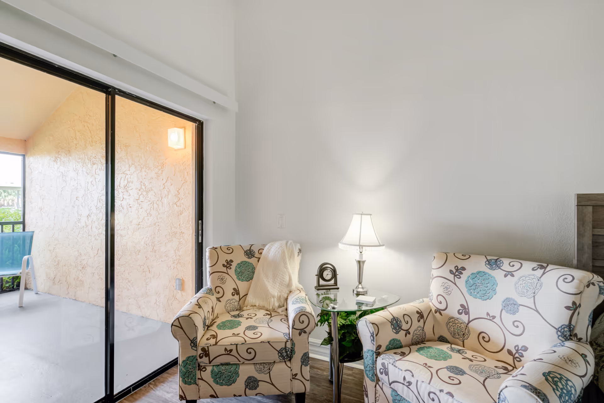 Two patterned armchairs with a glass side table and lamp in a bright living room.