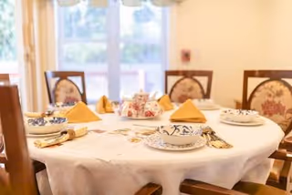 Round dining table set for a meal with folded yellow napkins in a bright dining room.