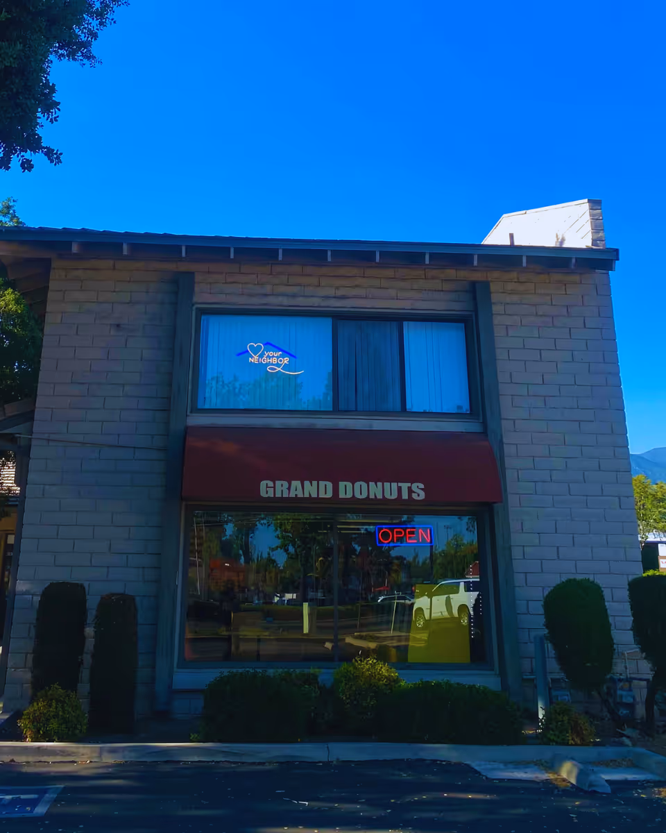 Front view of a two-story building with Grand Donuts storefront and open sign.