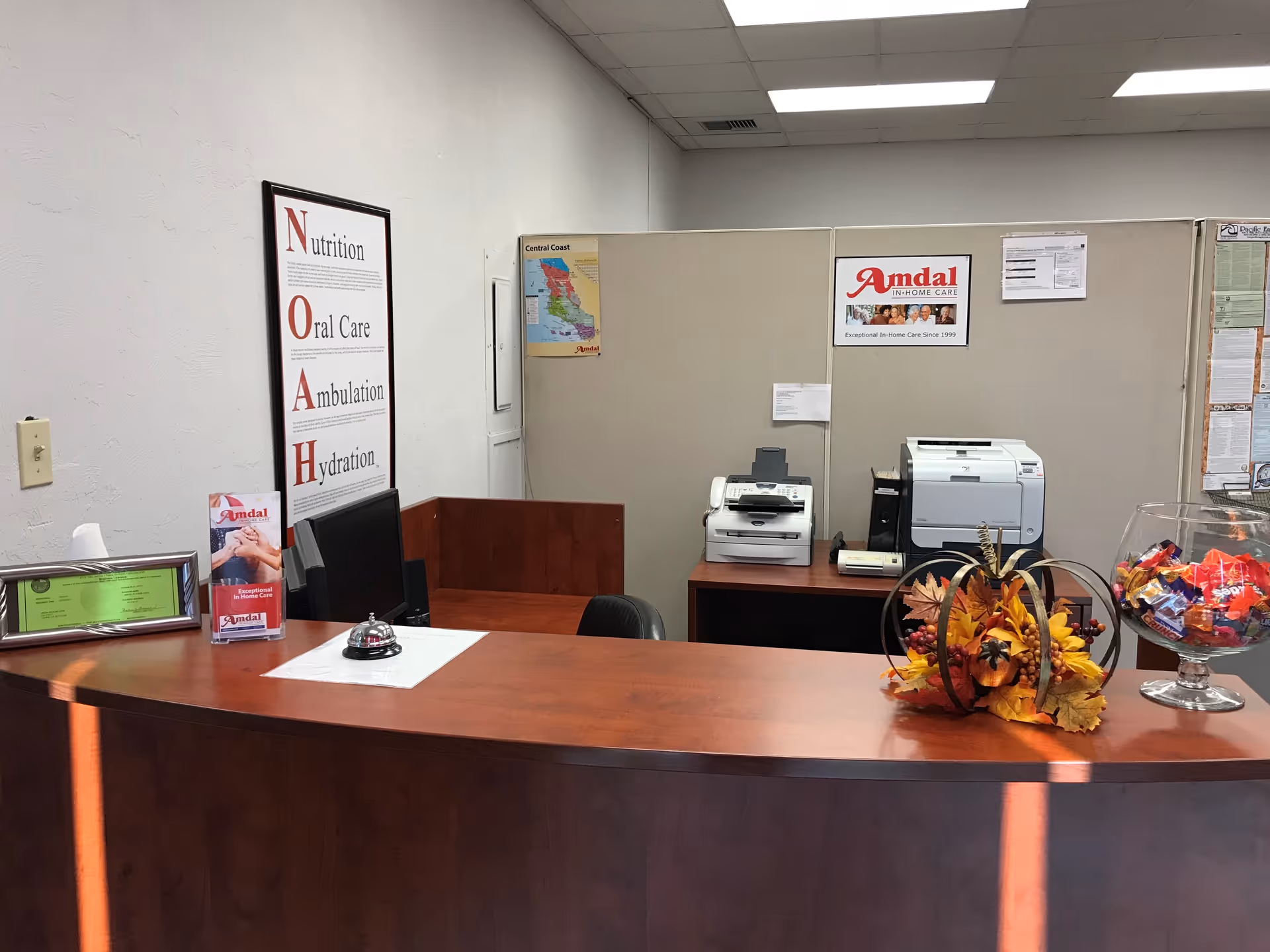 Reception area with curved wooden desk, posters, printers, and an autumn centerpiece at Amdal In-Home Care.