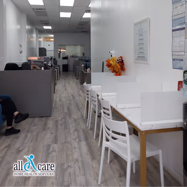 Office area inside a senior care facility with cubicles, desks, and white chairs along a hallway.
