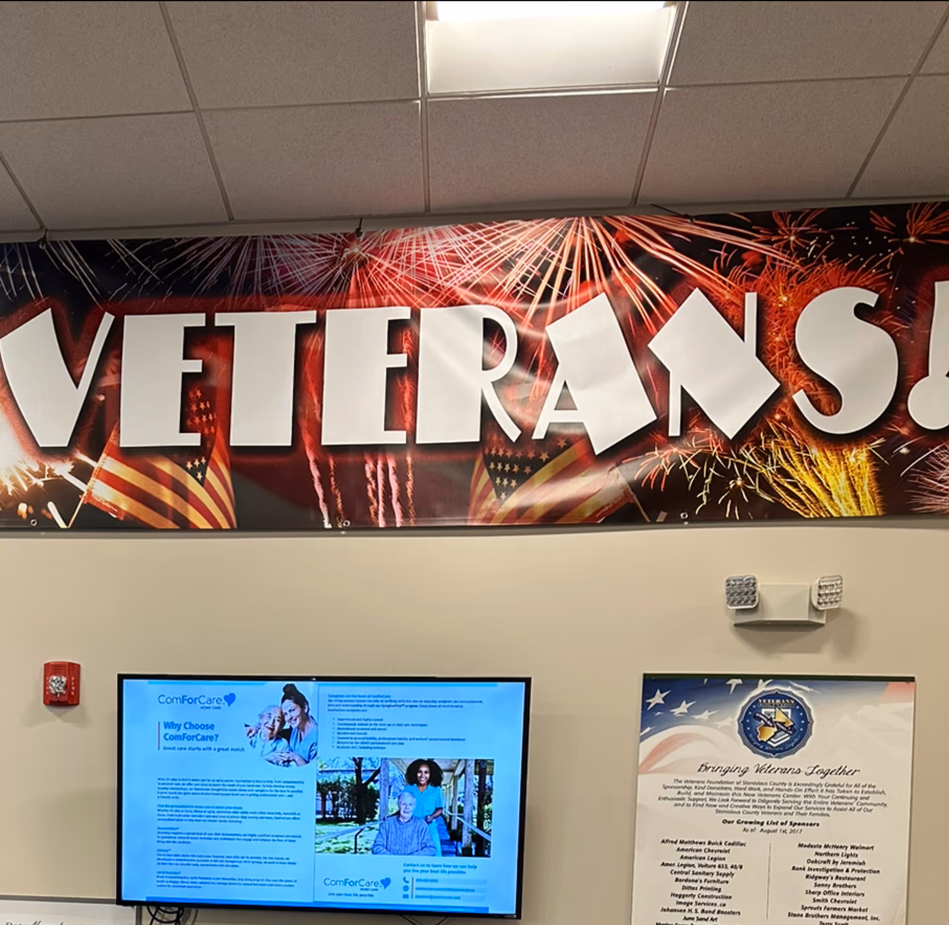 Indoor wall with a large 'VETERANS' banner, ceiling tiles, and a monitor displaying information.