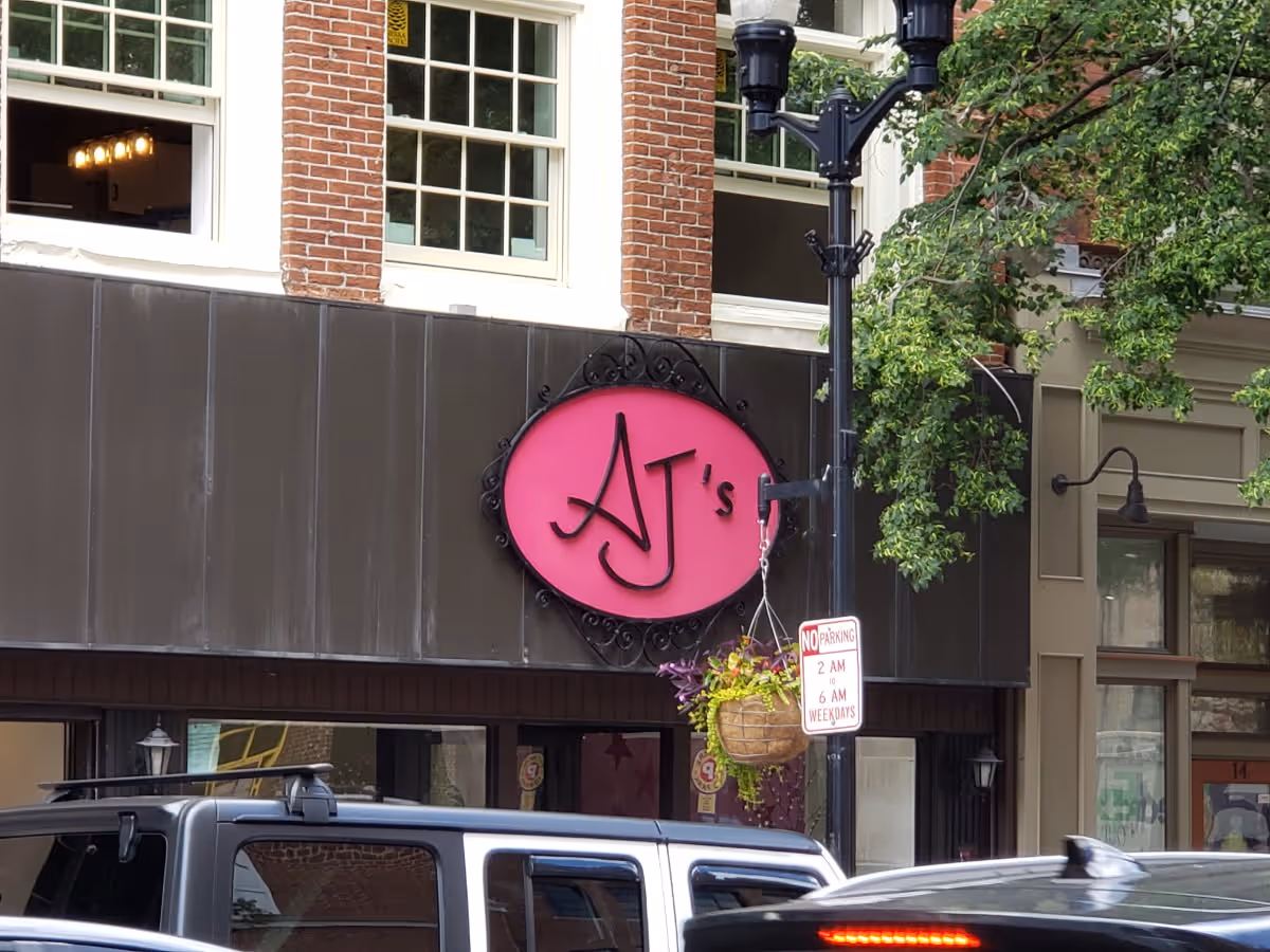 Exterior of a brick building with a pink circular AJ's sign and hanging flower basket