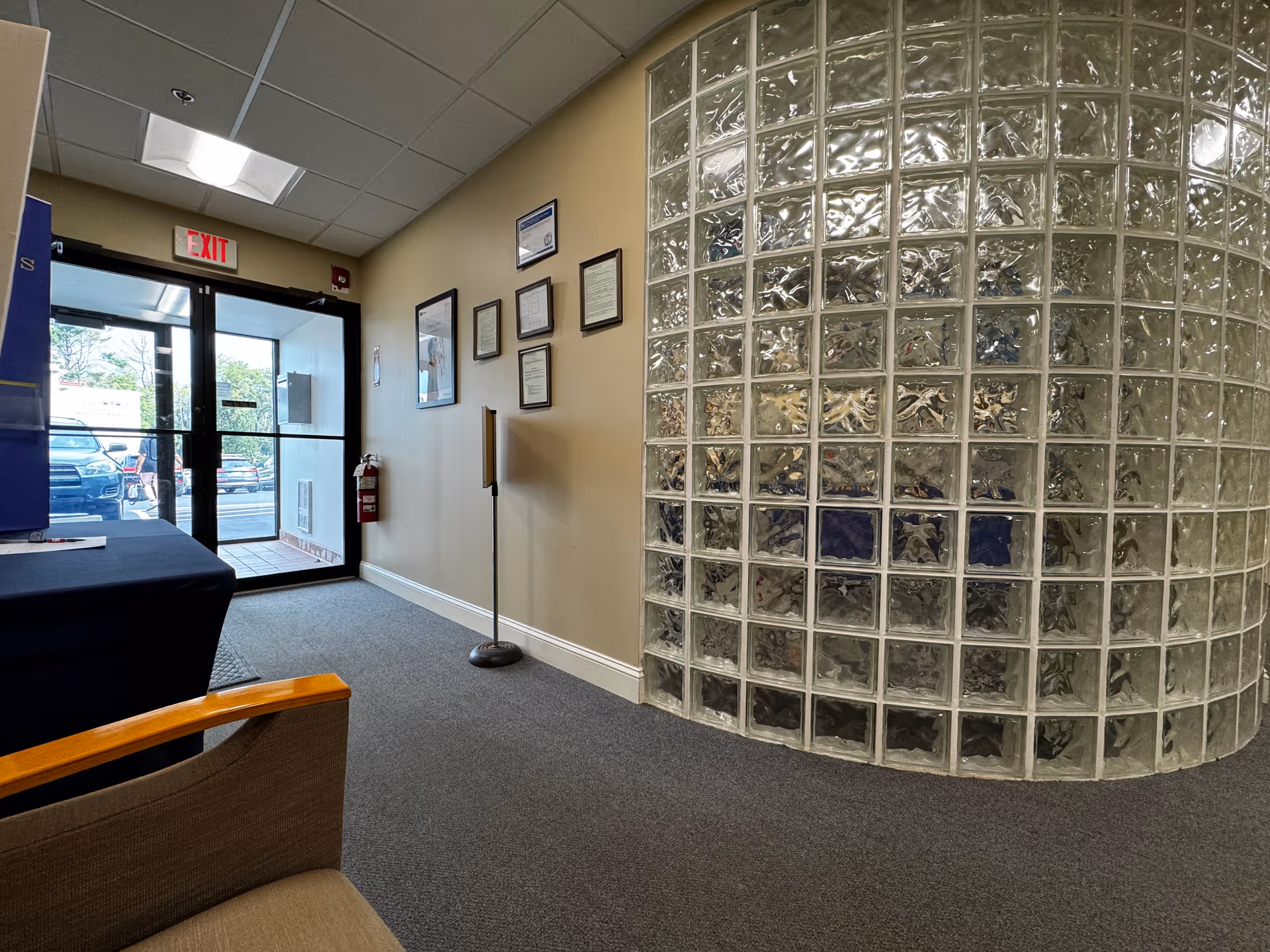 Interior lobby near the entrance featuring a curved glass block wall, exit door, and seating.