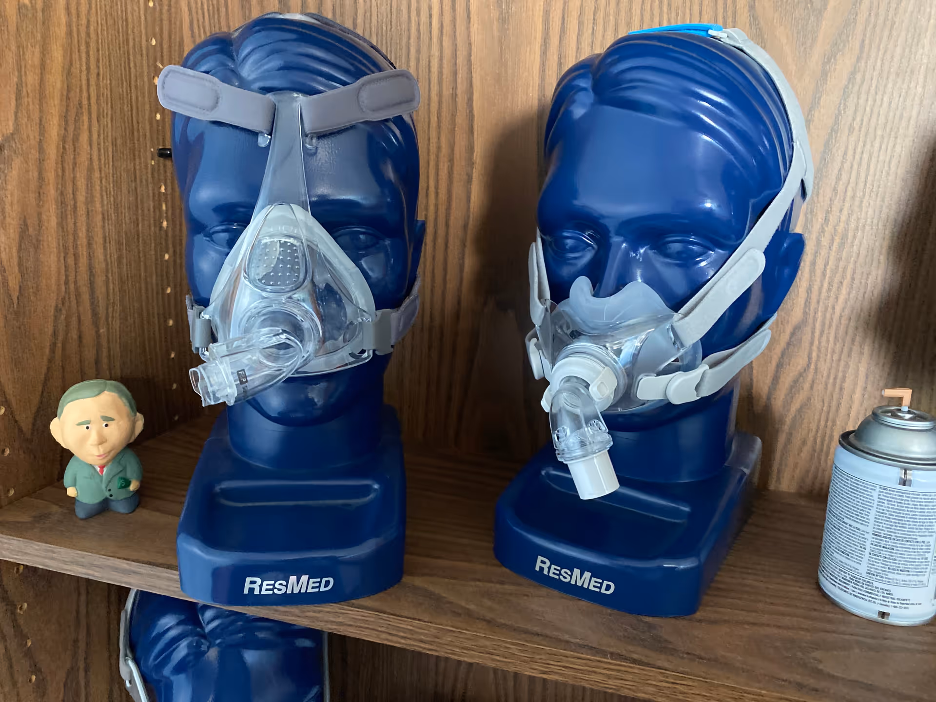 Two blue ResMed CPAP masks on a shelf with a small figurine and a spray can.