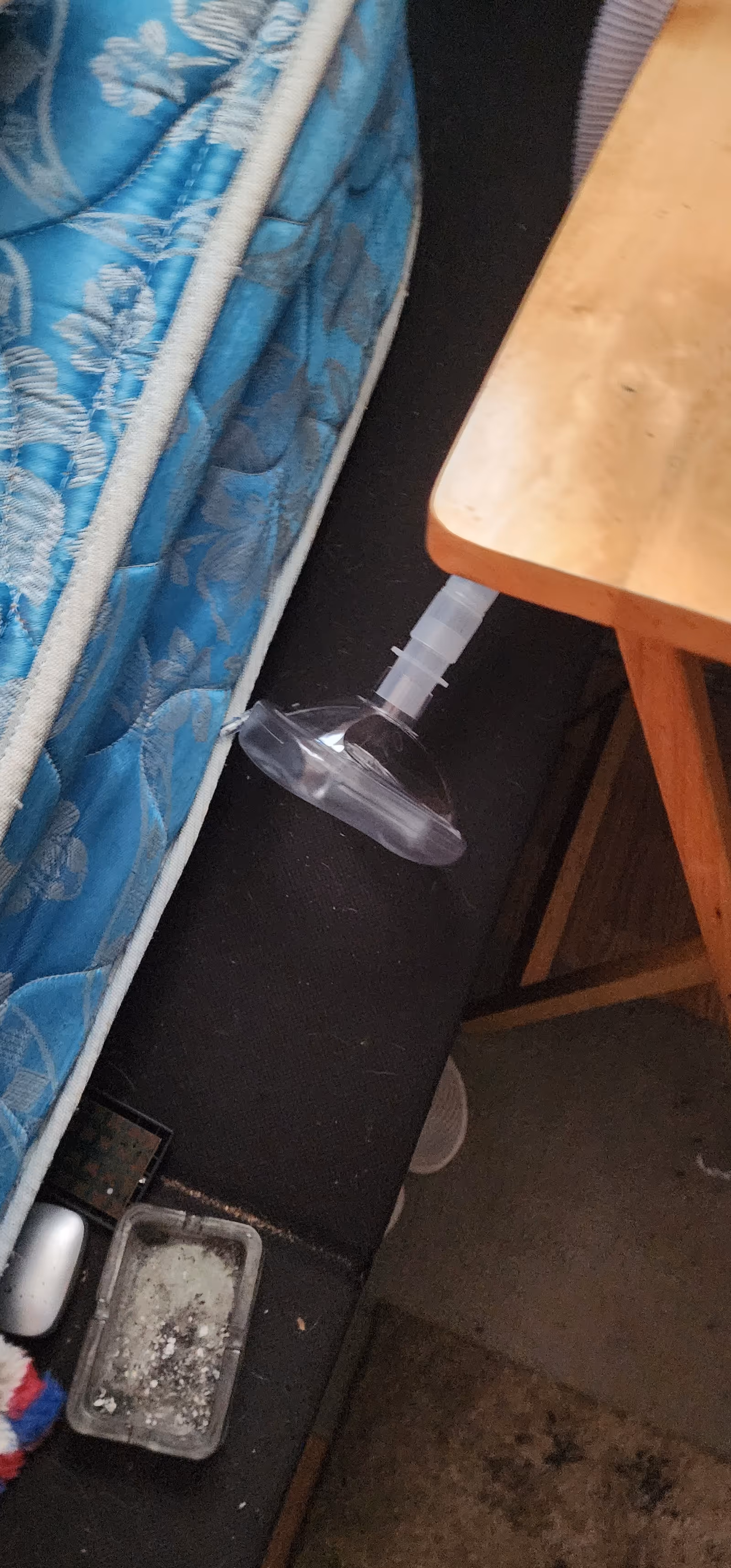 A blue-patterned mattress beside a wooden table with a suction cup device attached.
