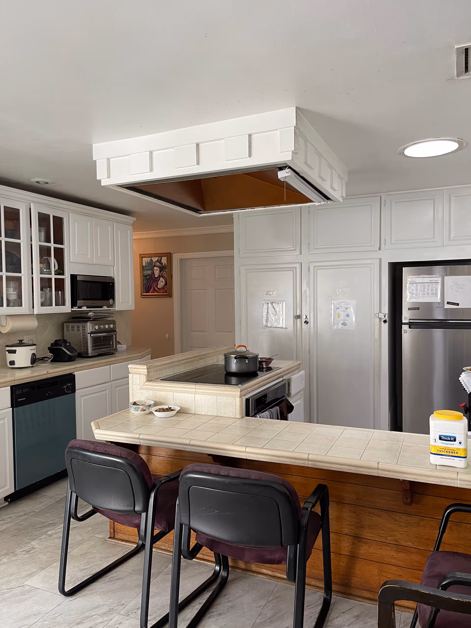 White kitchen with island, built-in appliances, and bar-height seating in a senior living facility.