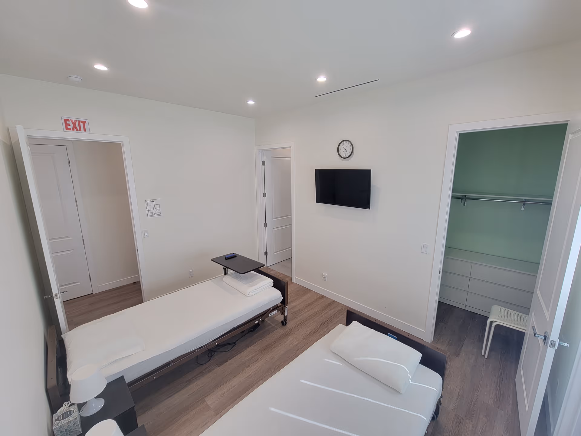 Two single beds in a bright, minimalist shared bedroom with a wall-mounted TV.