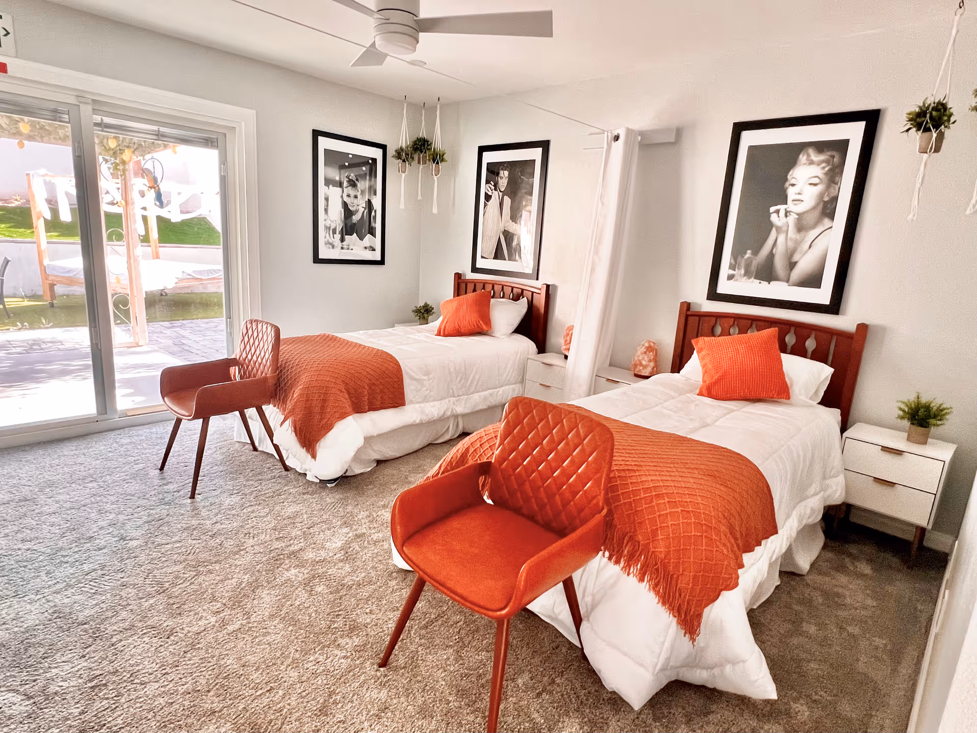 Two twin beds with orange throws and black-and-white portraits in a bright bedroom.