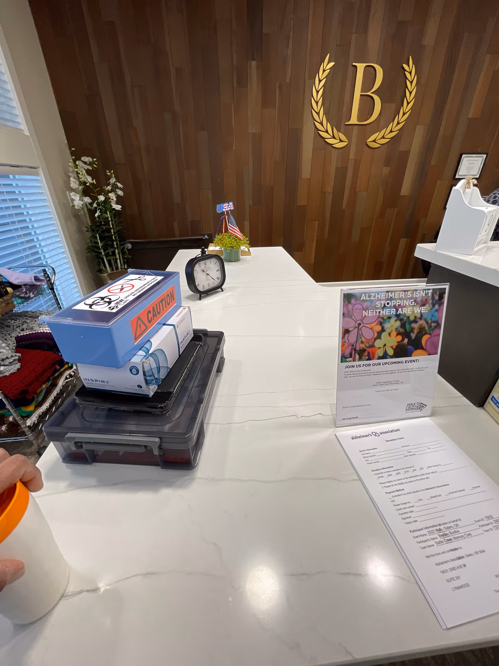 Reception desk with white countertop, wooden wall, and a decorative B emblem in the lobby.