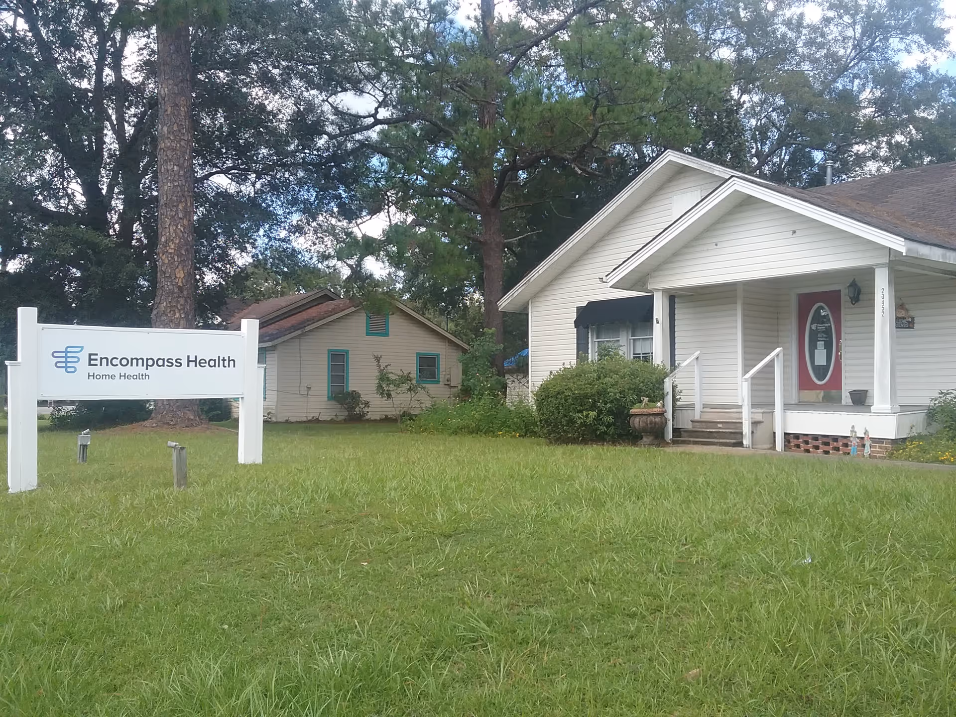 White, single-story building with front porch and Encompass Health sign on the lawn.