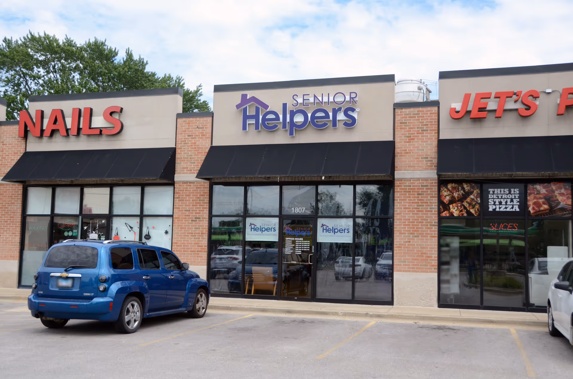 Exterior view of a shopping plaza with Senior Helpers, Nails, and Jet's Pizza storefronts.