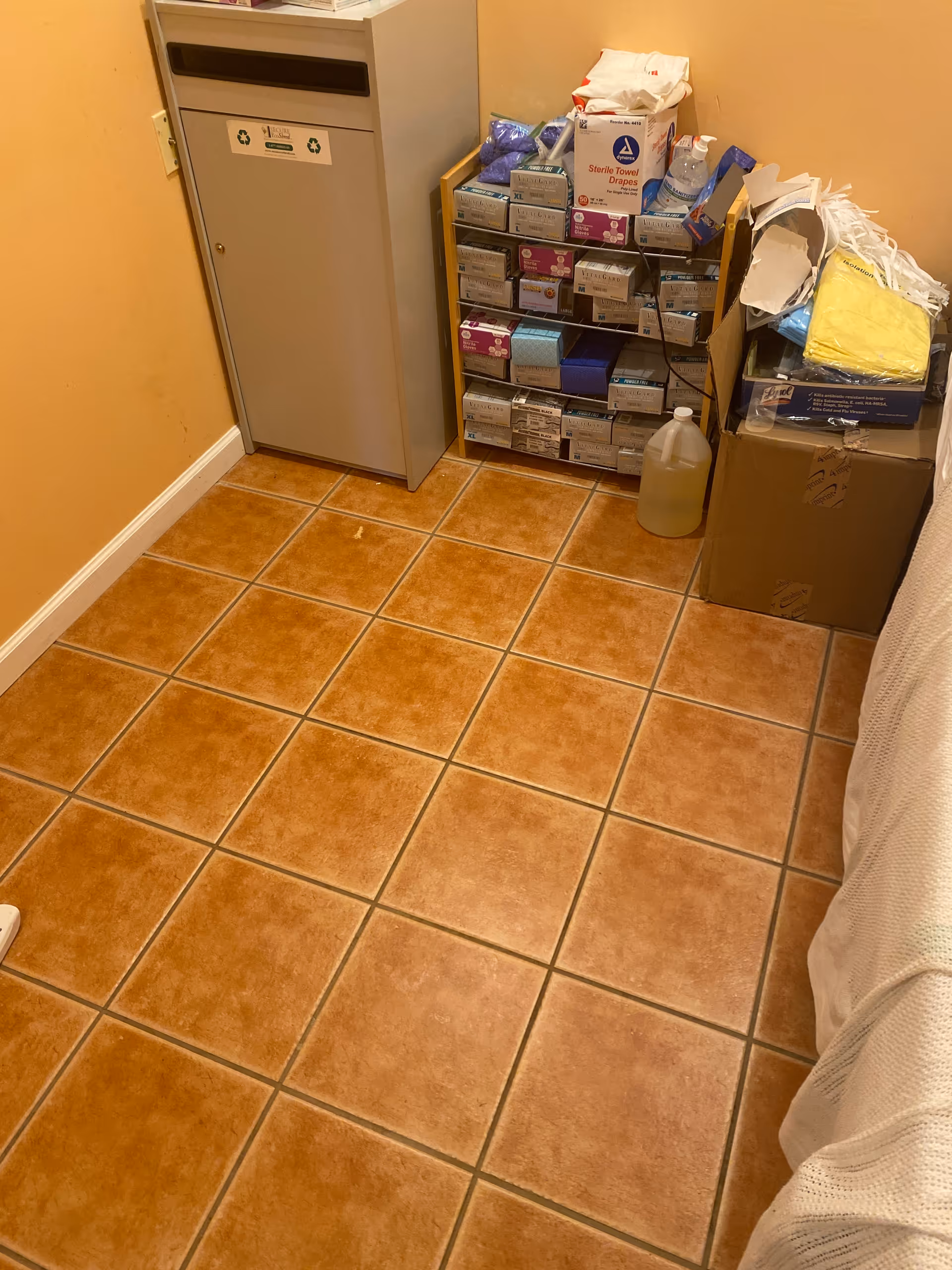 Narrow storage corner in an orange-tiled room with shelves of supplies and boxes.