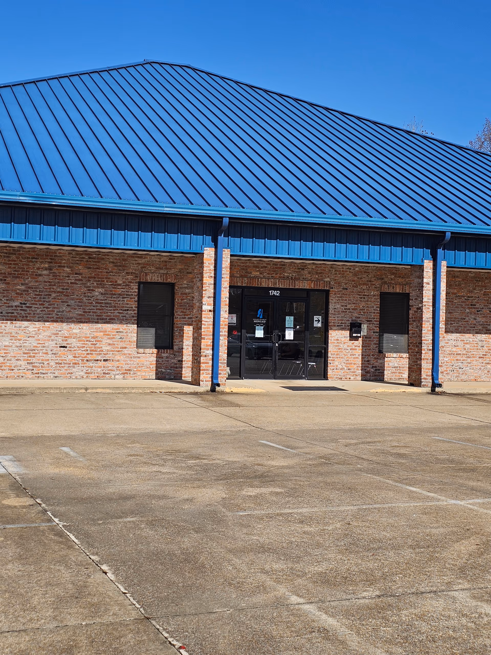 Brick building with a blue metal roof, glass entrance, and empty parking lot.