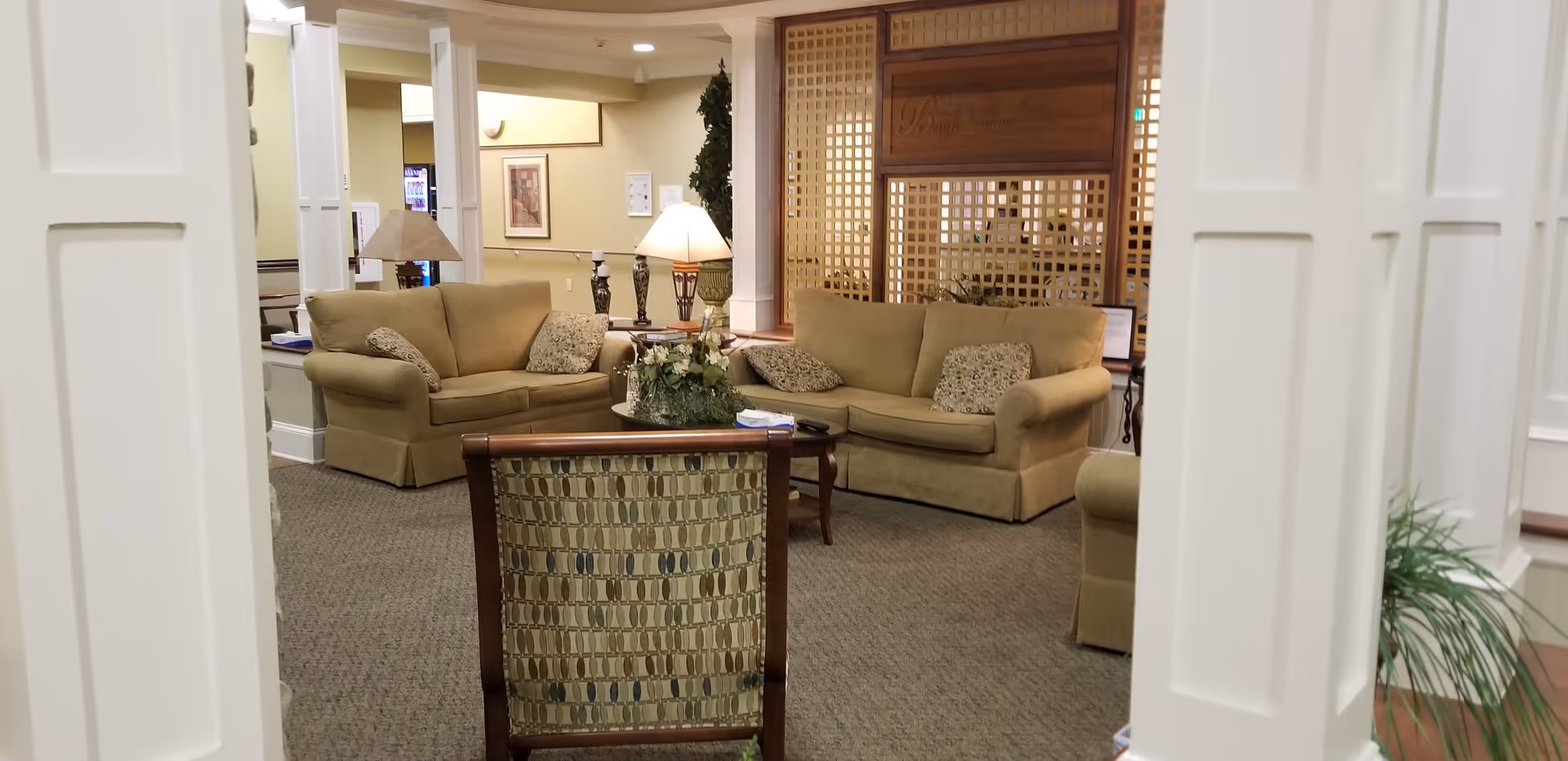 Reception-style lounge with beige sofas, coffee table, lamps, and a decorative lattice divider.