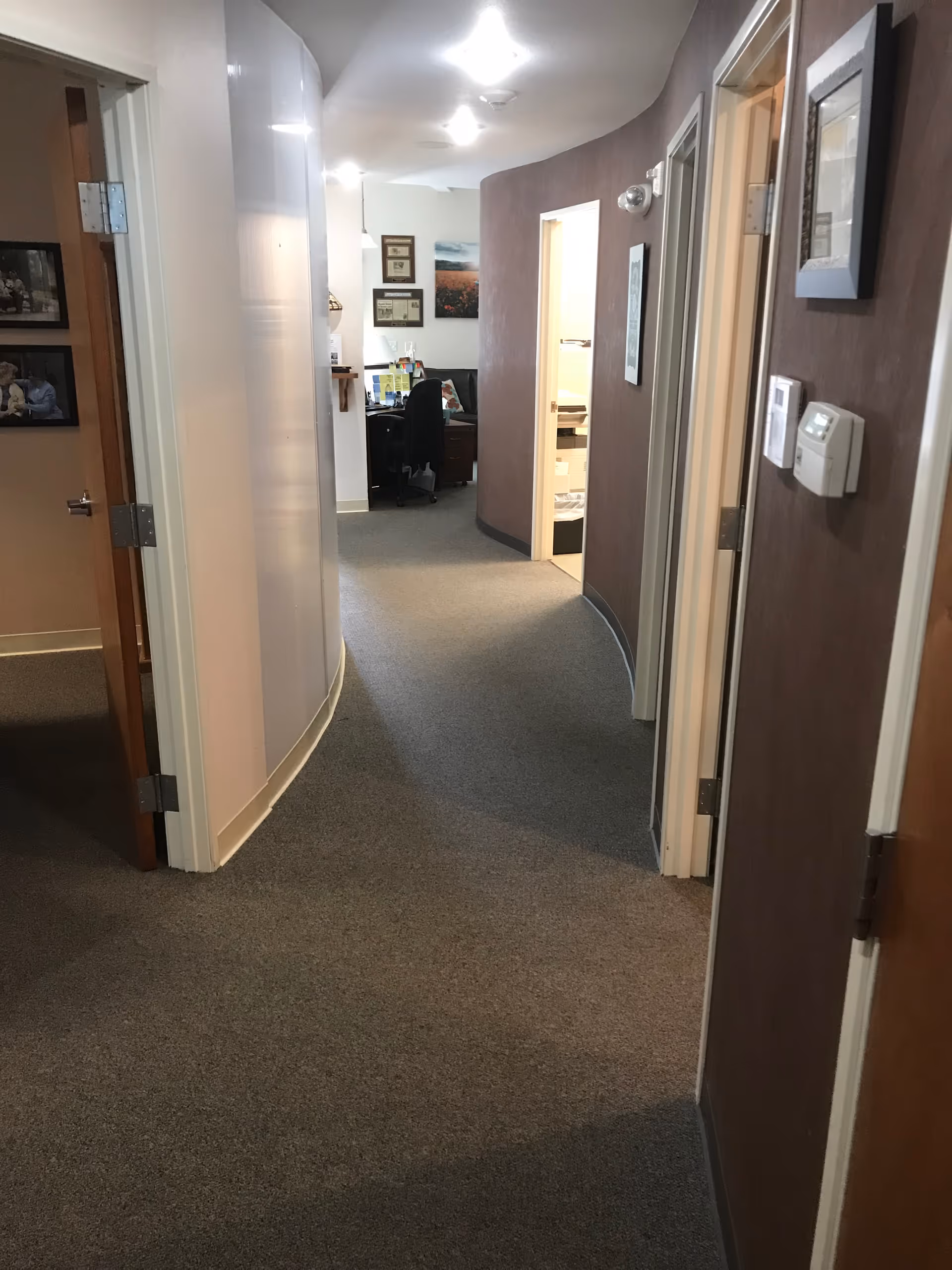 Interior hallway of a senior living facility with doors, carpet, and an office at the end.