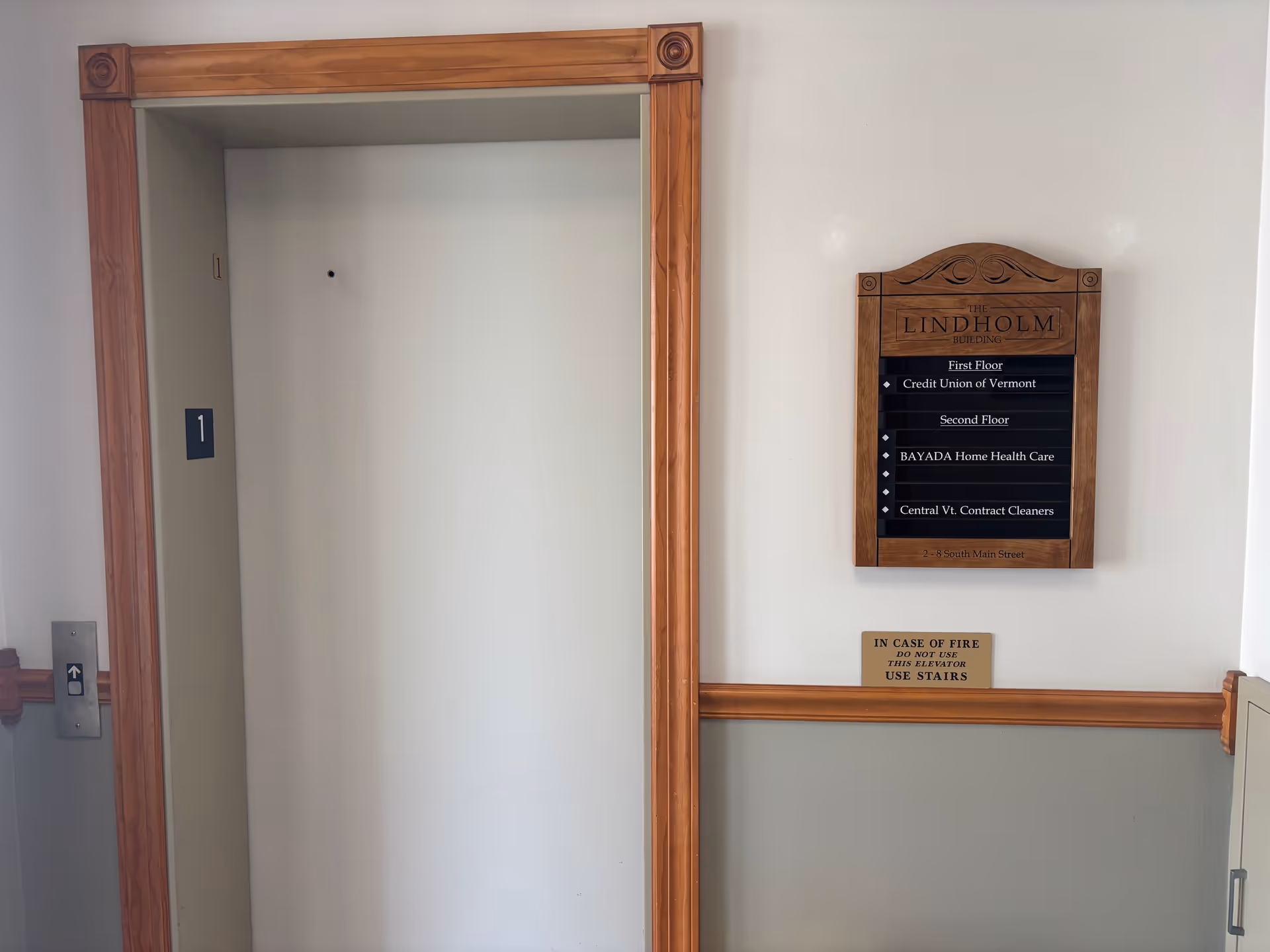 A hallway with an elevator door and a wooden directory sign on the wall.