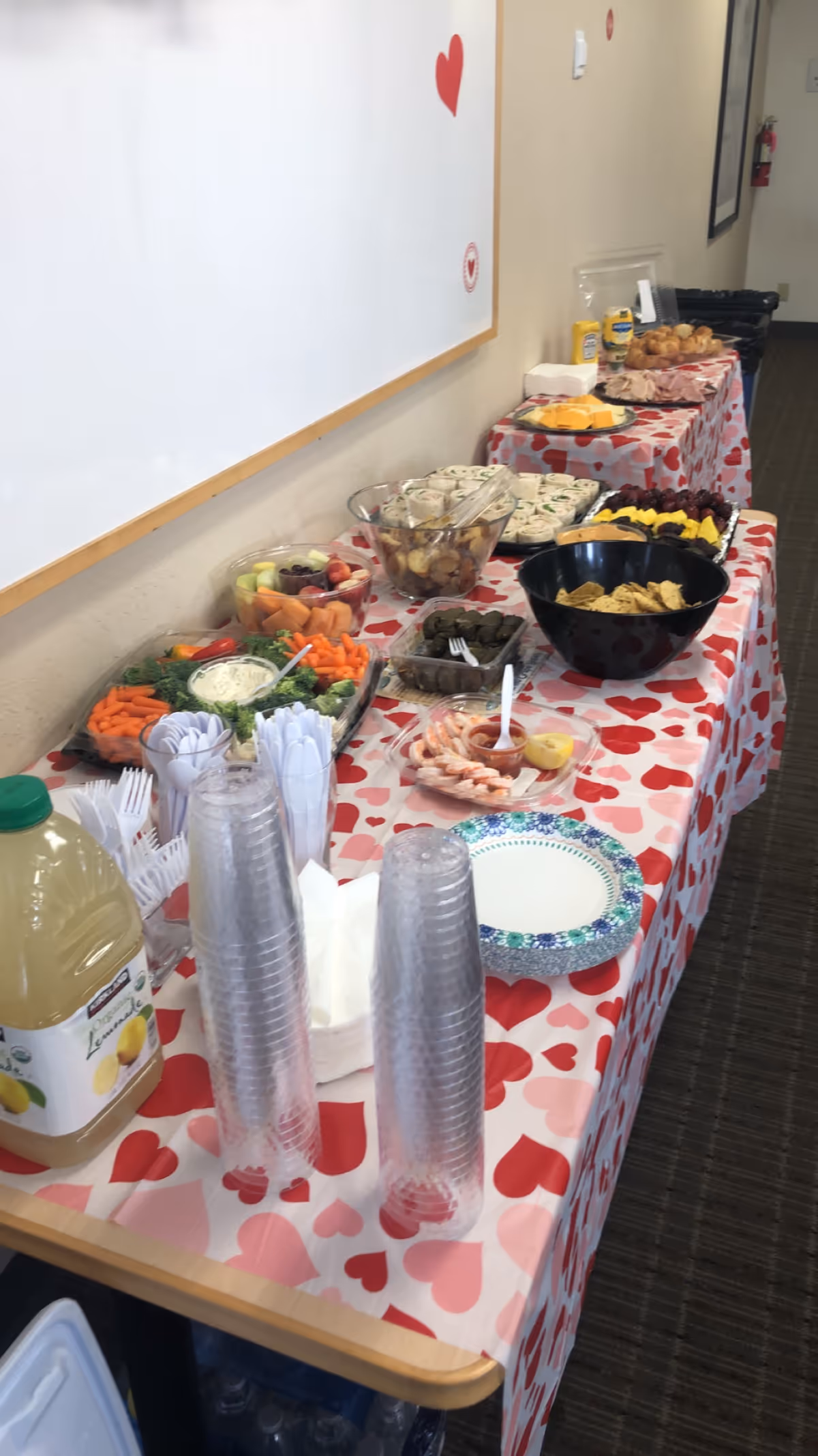 Buffet-style snack table inside a facility hallway with heart-patterned cloth, drinks, and snacks.