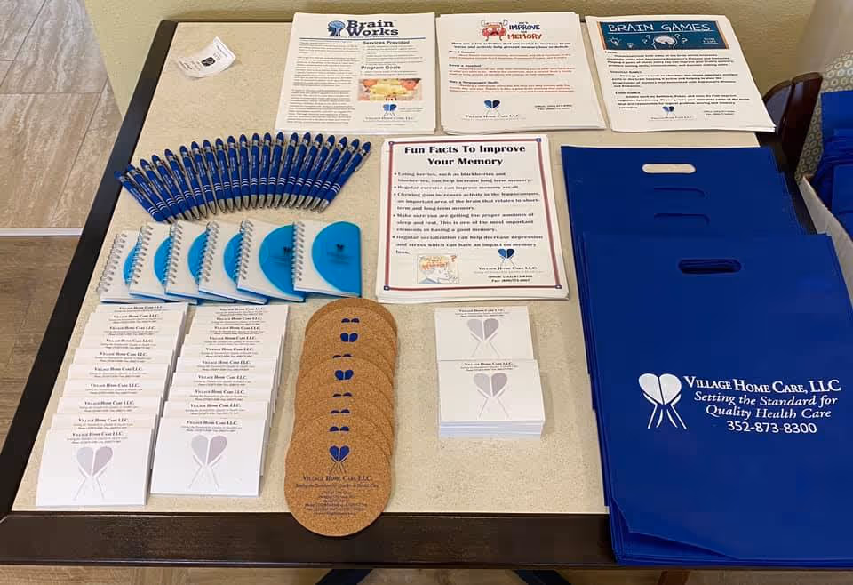 Promotional brochures, pens, and blue folders for Village Home Care LLC on a table.
