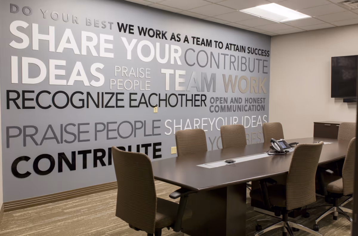 Interior conference room with a long table, chairs, and a large wall mural of words.