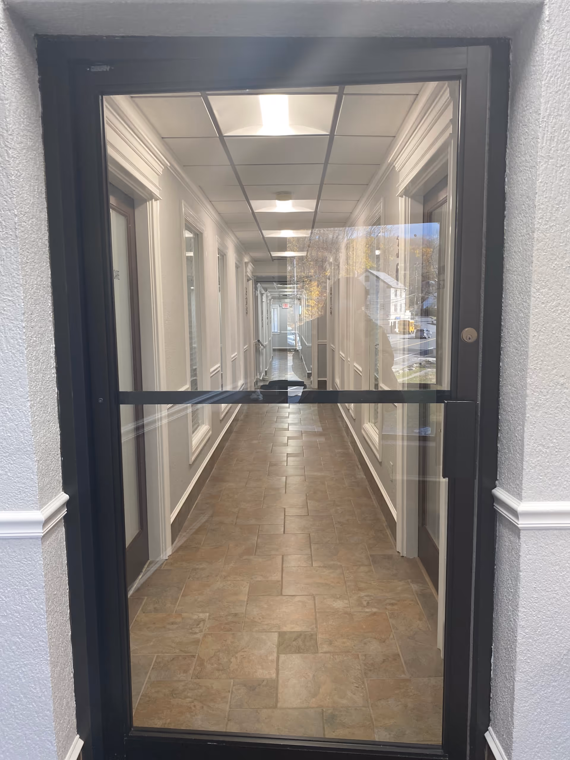 Glass-framed doorway opens to a bright interior hallway with tiled floor.