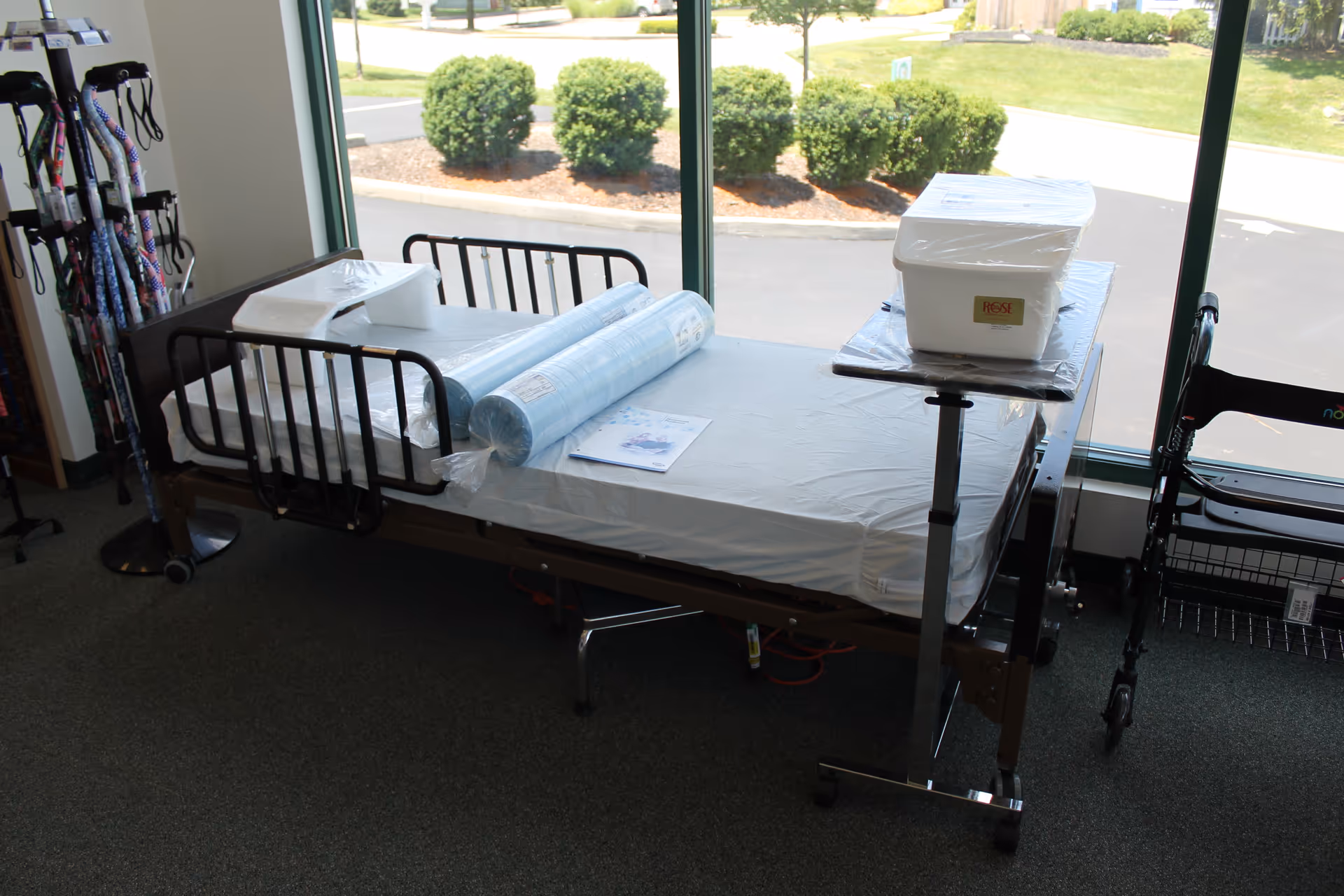 Hospital-style patient bed in a supply room with medical equipment and a window.