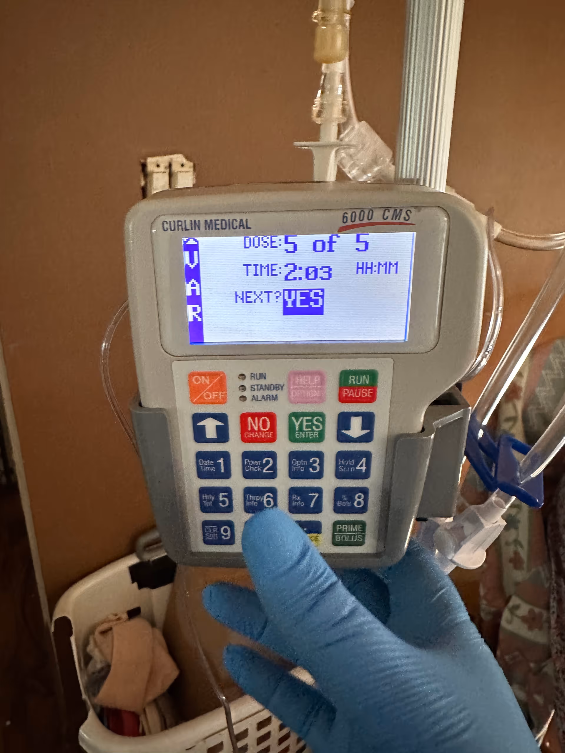 An indoor IV infusion pump is being adjusted by a gloved hand.