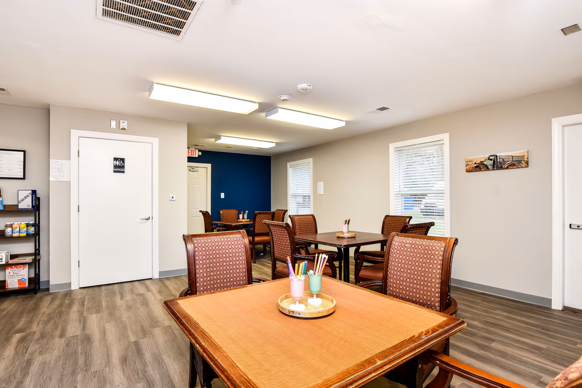 Bright communal dining room with several wooden tables and chairs.