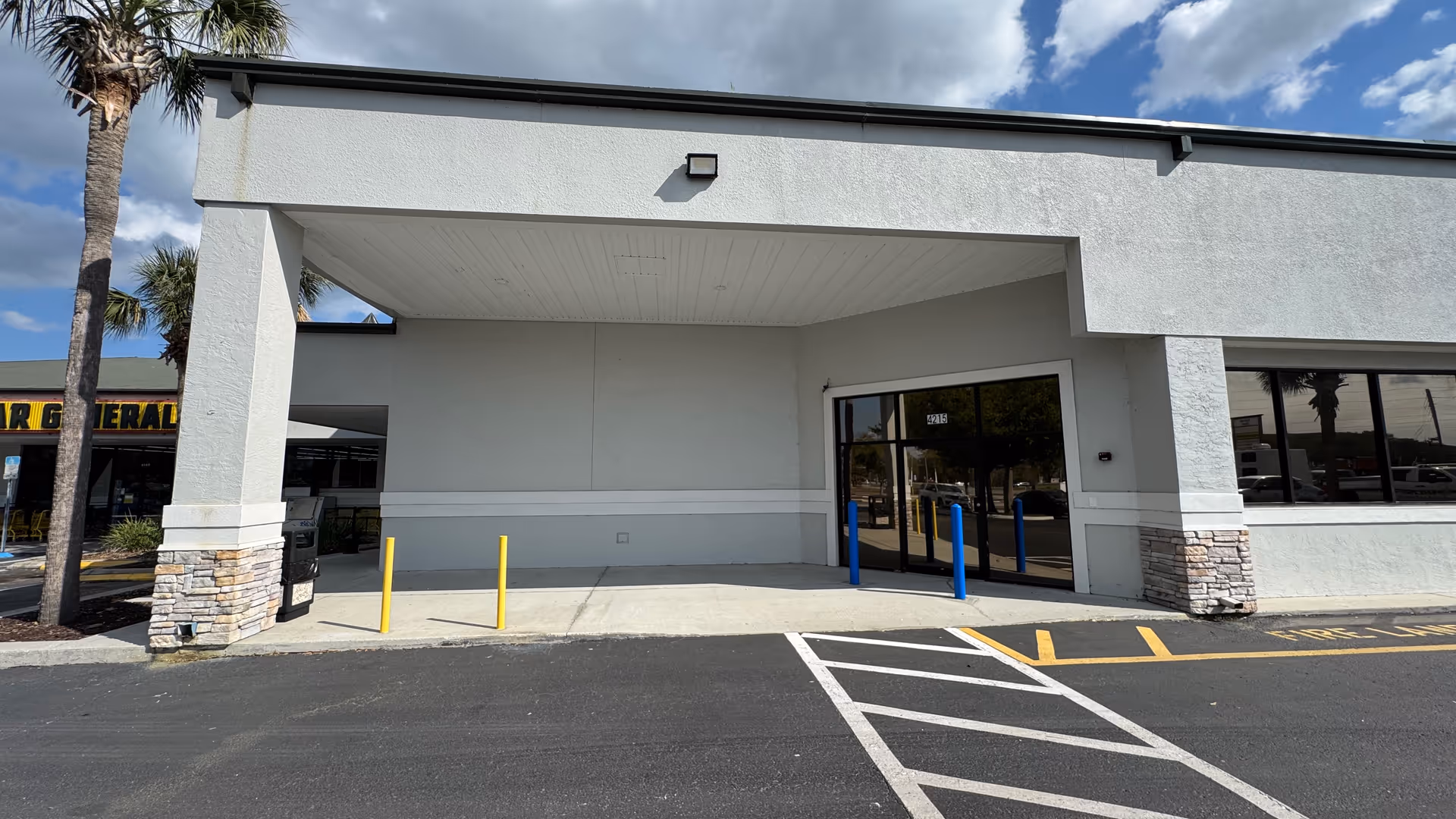 White stucco building entrance with covered drop-off and glass doors
