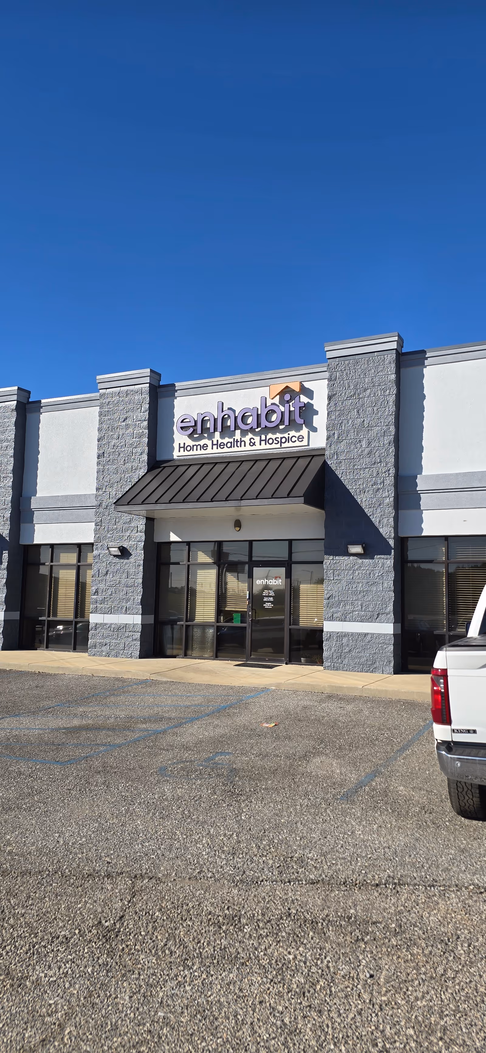 Front exterior of an Enhabit Home Health building with parking lot and clear blue sky.
