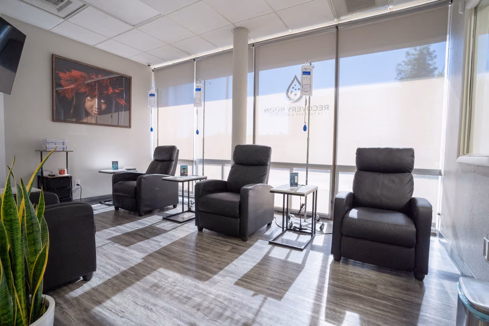 Sunlit interior with four black reclining chairs and IV poles near windows.