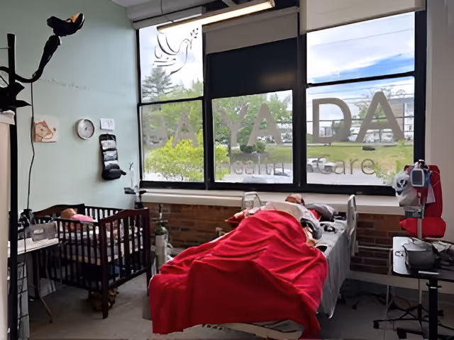 Hospital-style pediatric treatment room with a bed, red blanket, crib, and medical equipment.