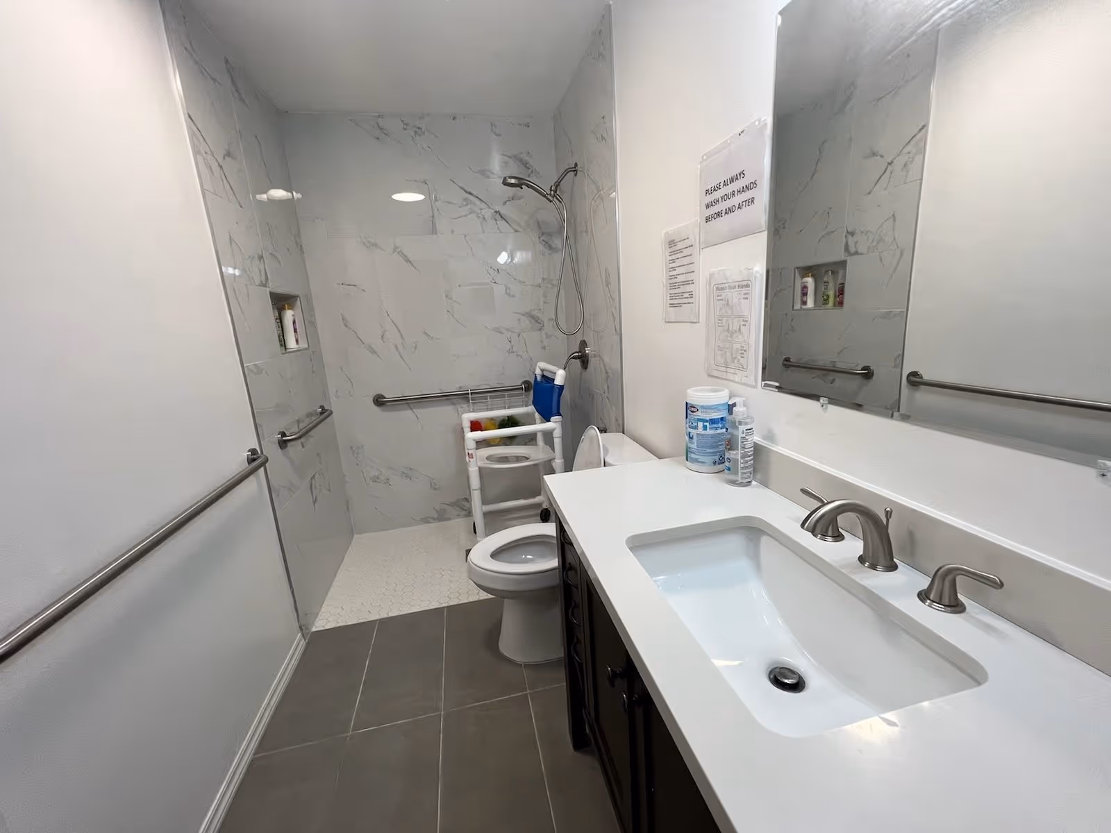 Accessible bathroom with a walker, grab bars, toilet, shower, and marble walls.