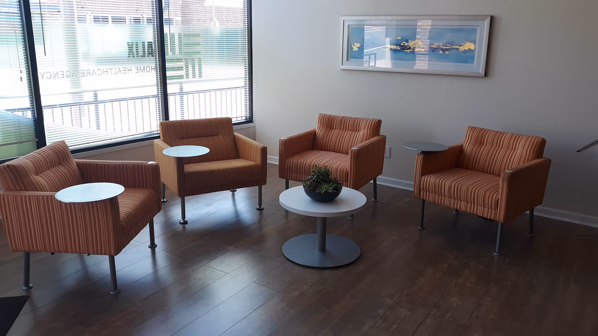 Modern senior living lounge with orange striped chairs around round tables by windows.