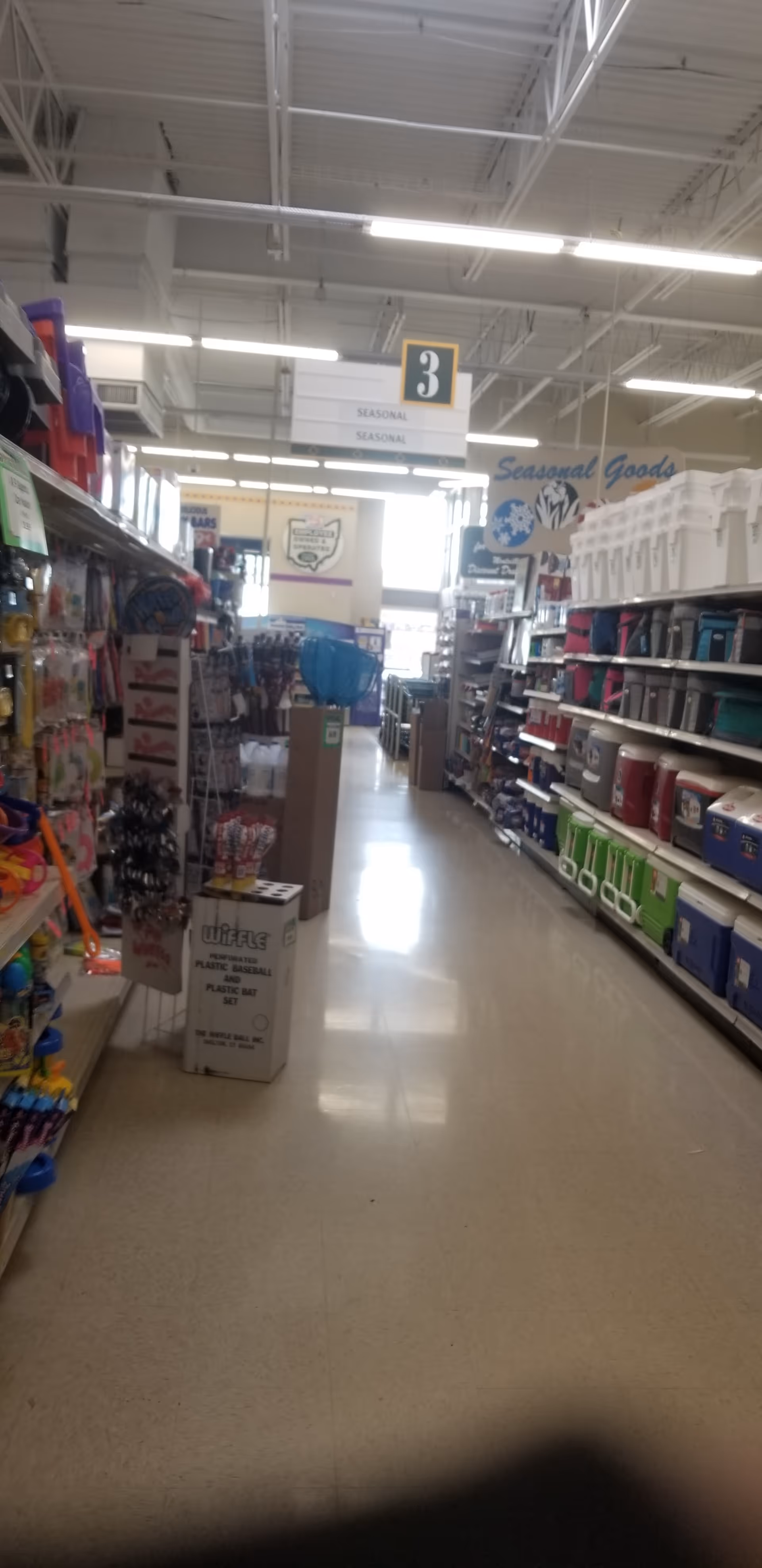 Long store aisle with tall shelves stocked with household and seasonal goods.