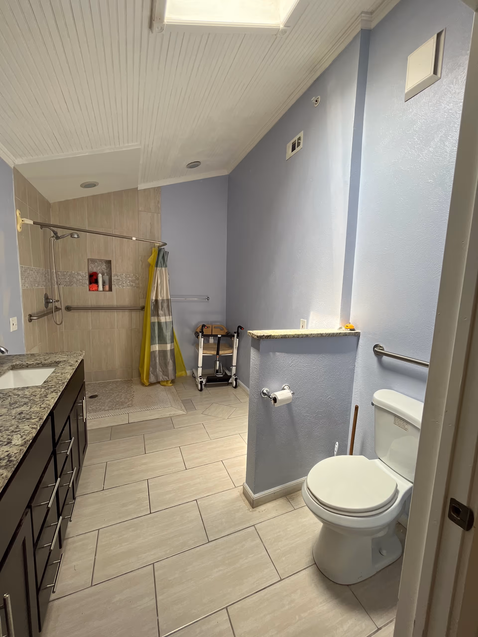 Accessible bathroom with a tiled shower, grab bars, toilet, and granite countertop vanity.