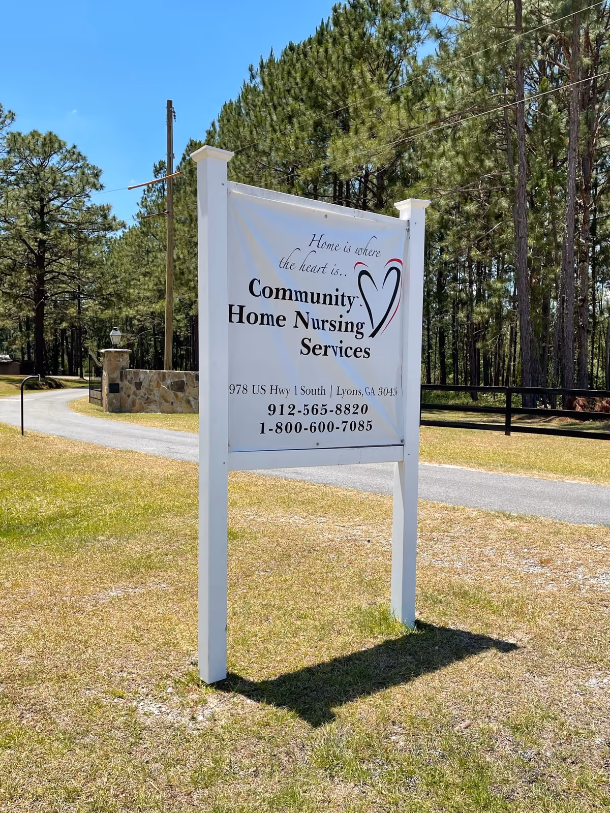 Outdoor sign for Community Home Nursing Services amid tall pines beside a rural road.