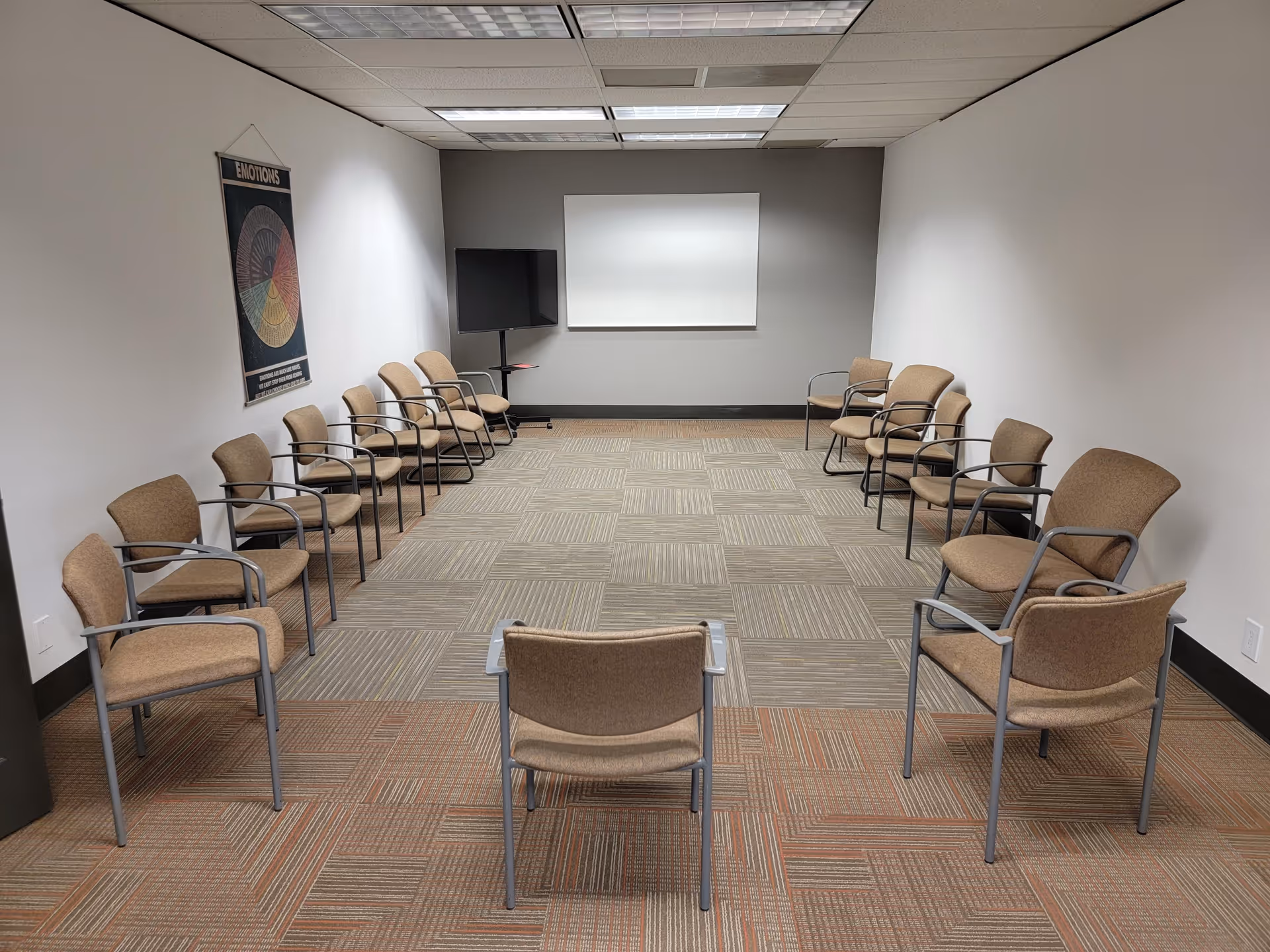 A conference room with dozens of brown chairs arranged around a center area facing a whiteboard.