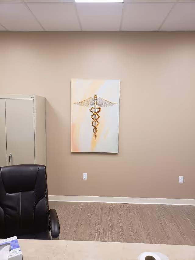 Office-like interior with beige walls, a caduceus painting, cabinet, and leather chair.