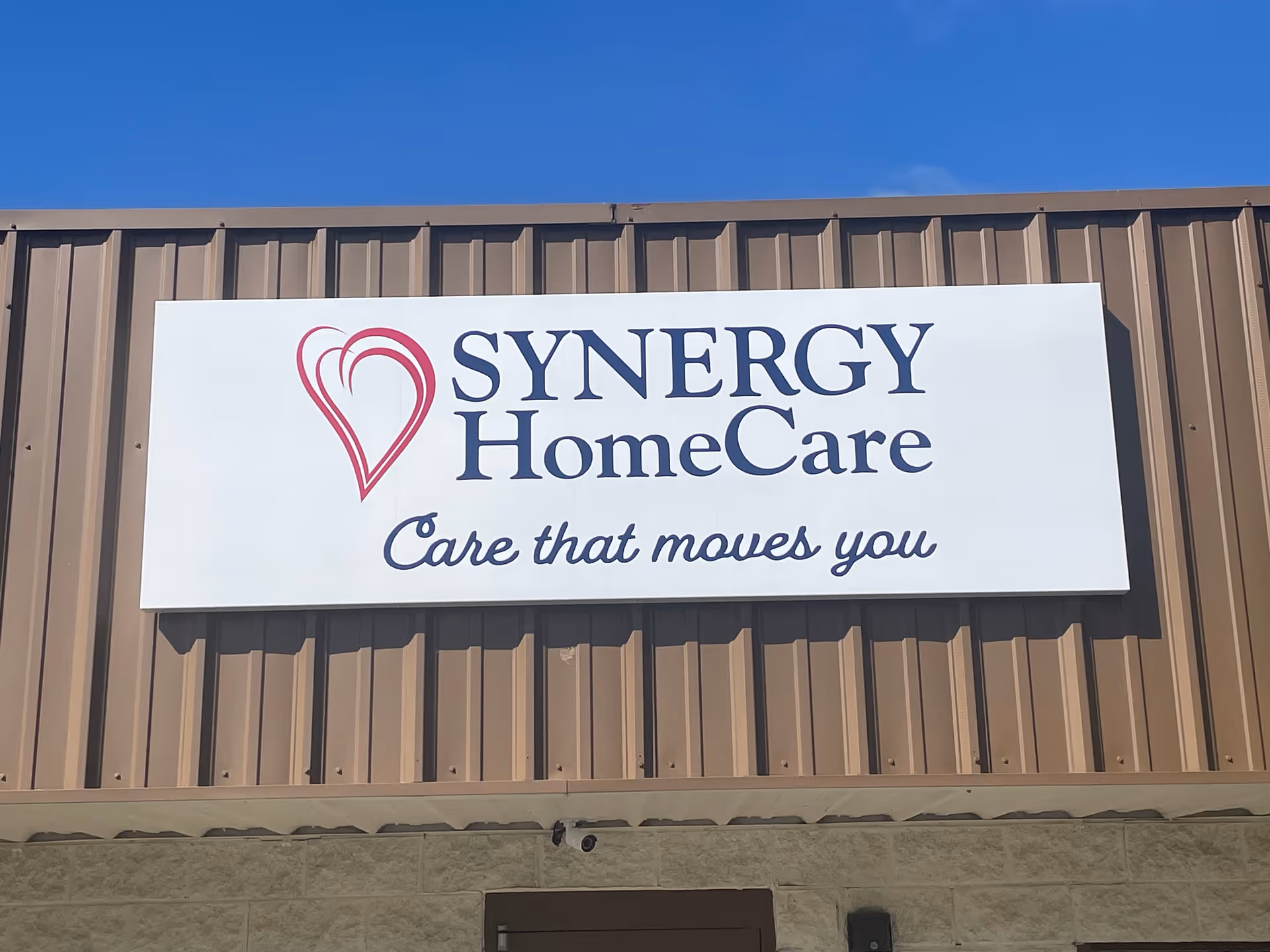 Exterior view of a SYNERGY HomeCare sign on a brown metal building.