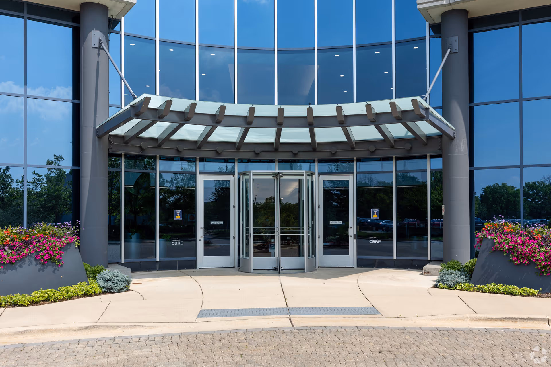 Modern glass-front entrance with a curved canopy and colorful planters outside.