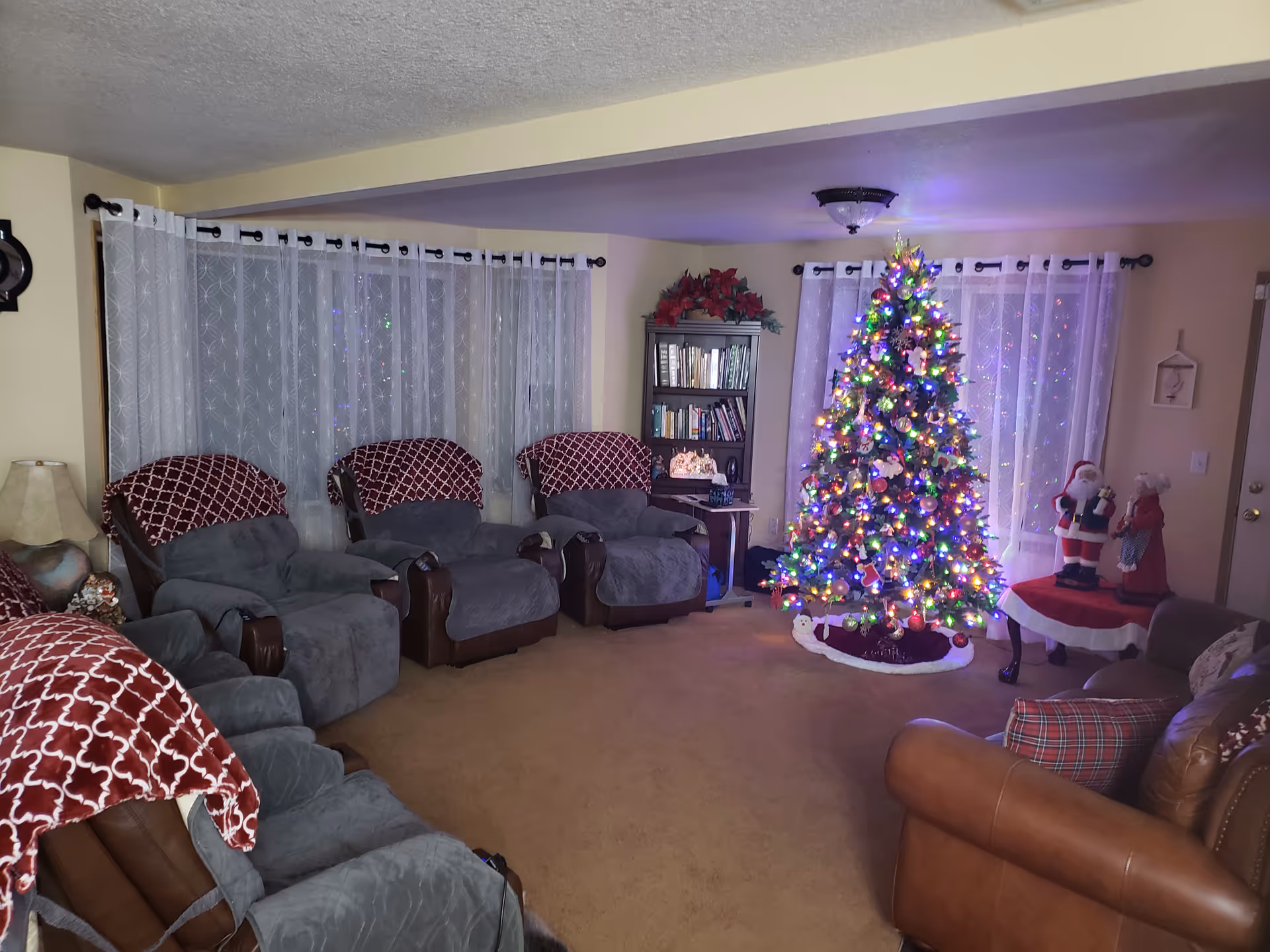 Cozy living room with a large Christmas tree, recliners, and festive decorations.